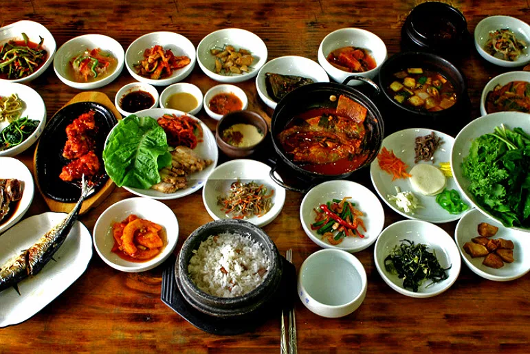 A traditional Korean set meal spread across a restaurant table, with rice, stew, and many side dishes. Chopsticks rest by the rice bowl. Photo: Traveli
