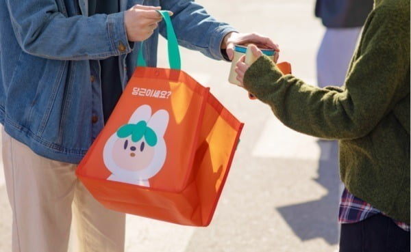 A face-to-face handoff of a Karrot-branded bag between two neighbors. Photo: KED Global