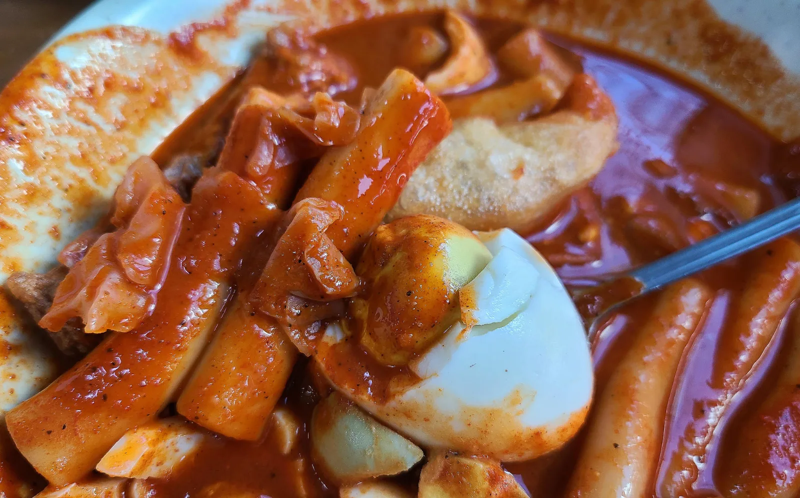 A close-up of tteokbokki in a deep red, spicy sauce with rice cakes, cabbage, a boiled egg and a fried dumpling. Photo: JoongAng Ilbo
