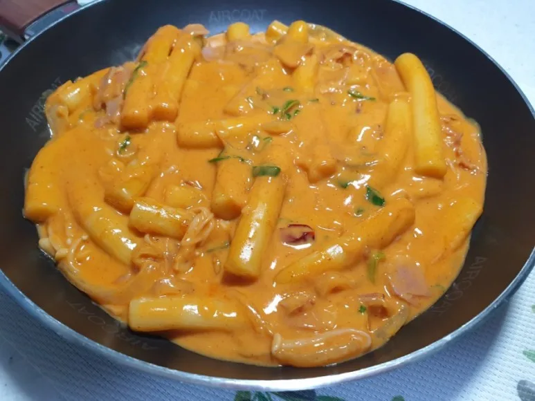 A plate of rosé tteokbokki, rice cakes in a creamy pink sauce topped with grated cheese and parsley. Source: Wtable